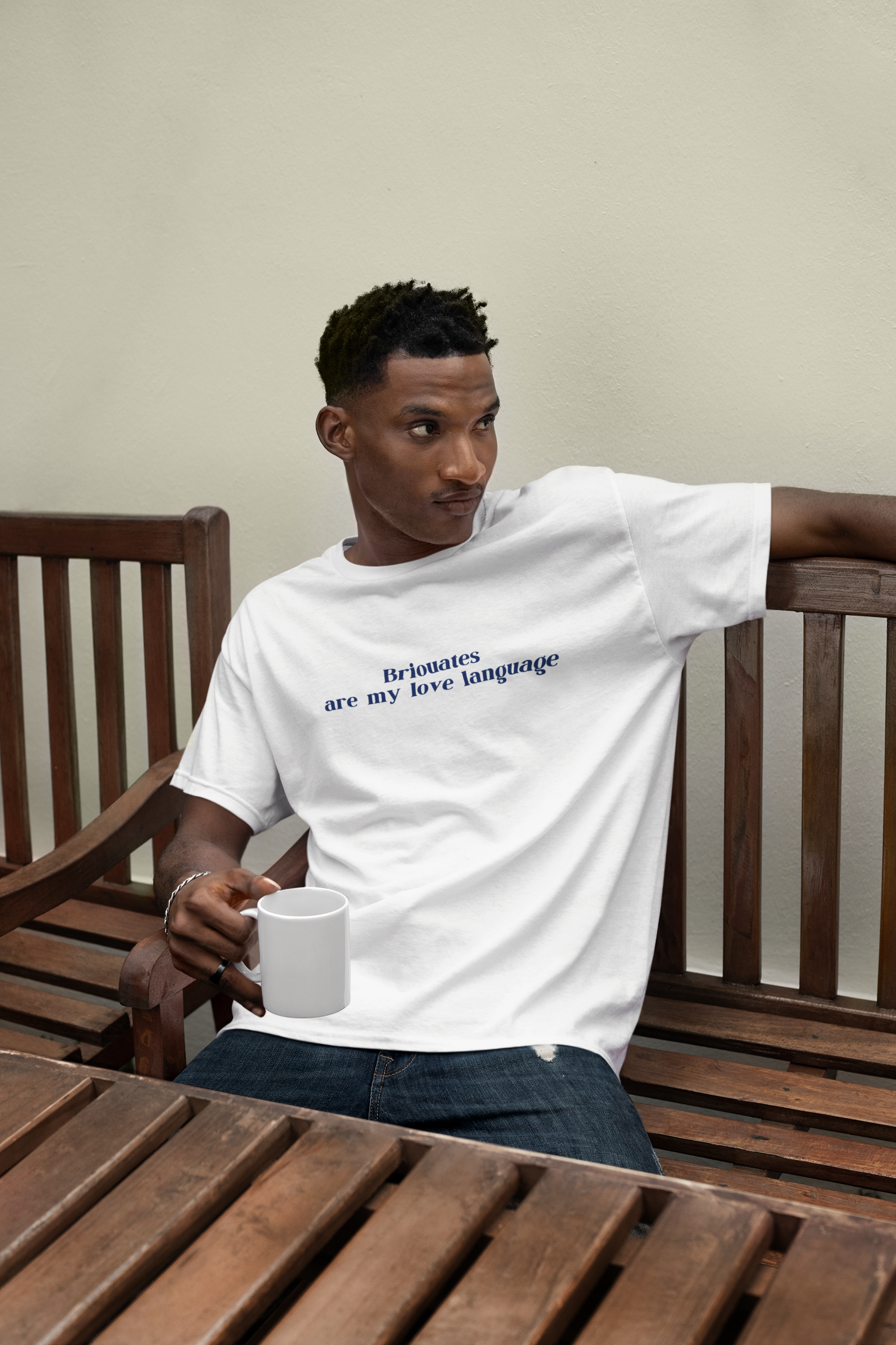 T-shirt featuring a man holding a coffee mug while sitting on a bench. Relaxed and casual look, perfect for cozy outdoor moments and everyday fashion