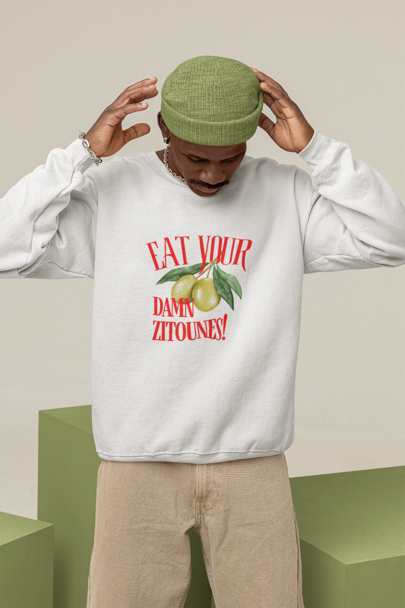 Model wearing the "Eat Your Damn Zitoune!" sweatshirt in white, showcasing playful North African streetwear.