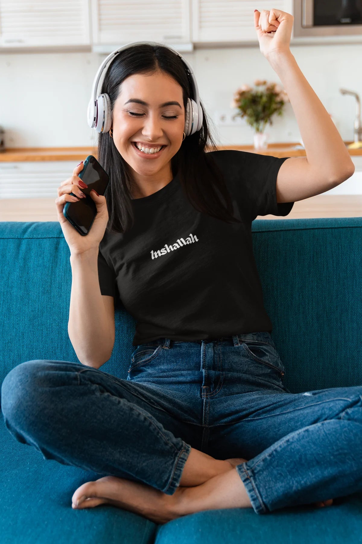 Woman enjoying music while wearing an 'Inshallah' T-shirt by Yallah You. Cozy indoor vibe with a relaxed and stylish Moroccan-inspired design