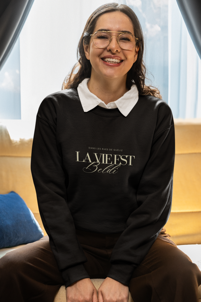 Woman in “La Vie Est Beldi” Sweatshirt Relaxing Indoors